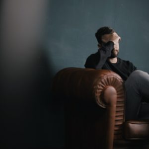 Man sits on a couch with his head in his hand as he learns more about addiction and how treatment can help.