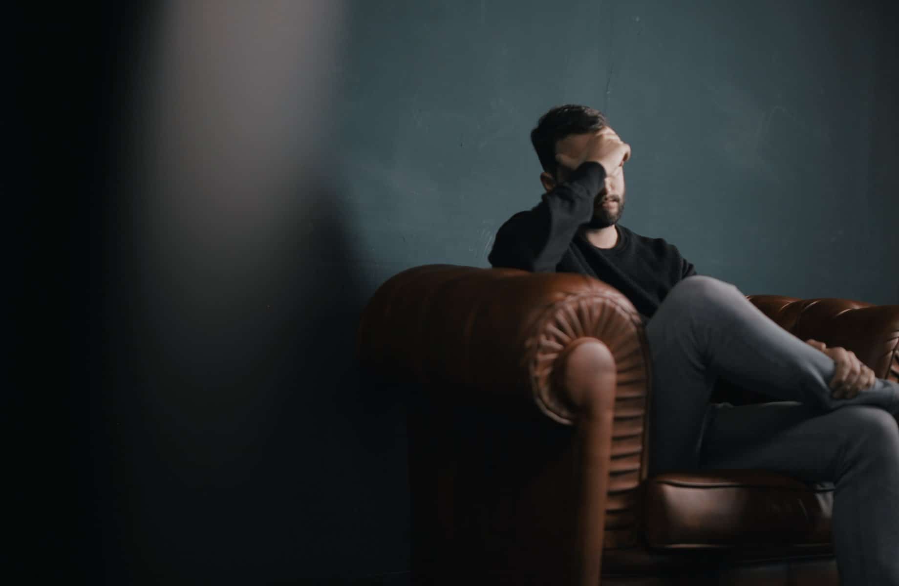 Man sits on a couch with his head in his hand as he learns more about addiction and how treatment can help.